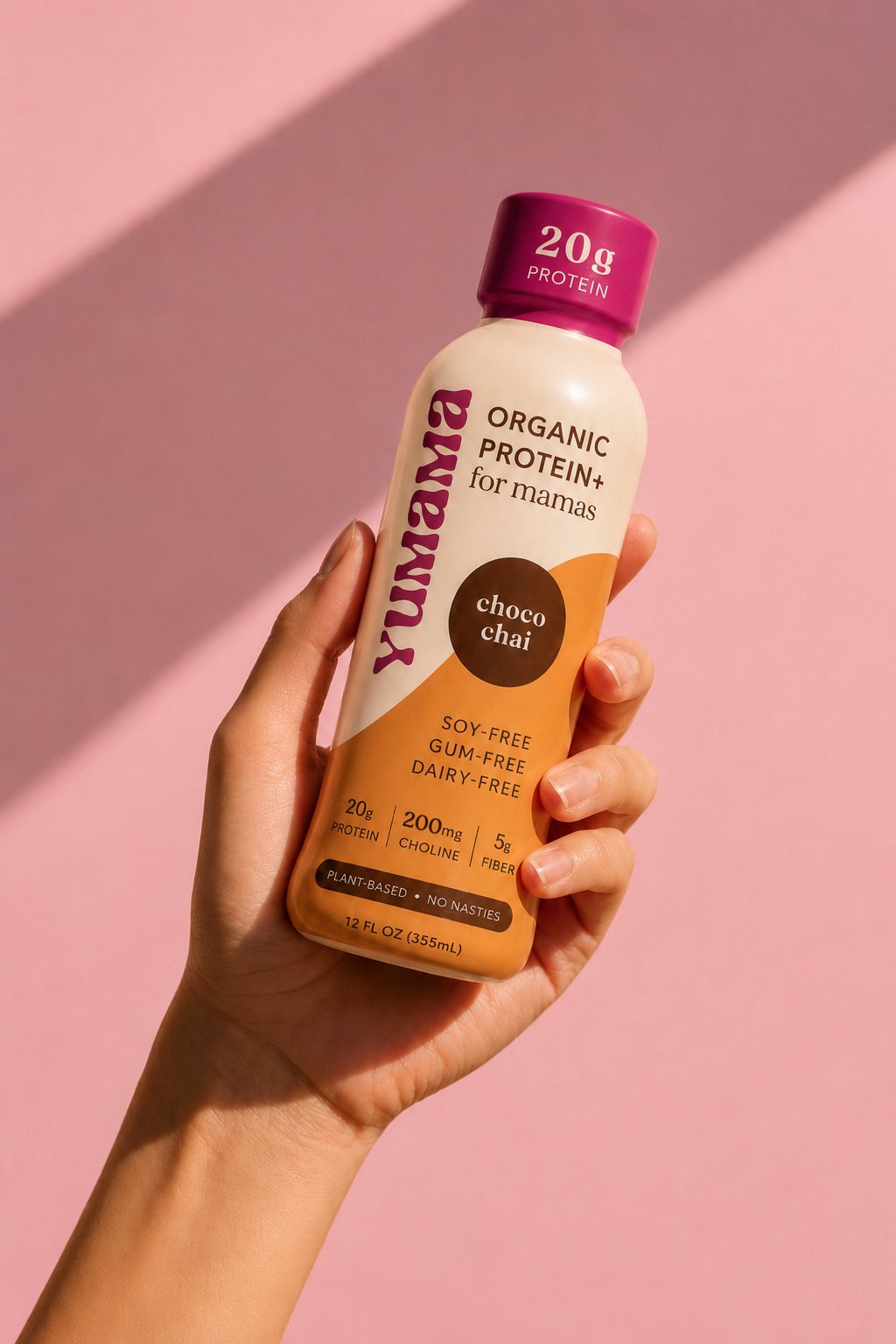 A hand holding a Yumama Choco Chai bottle against a pink background