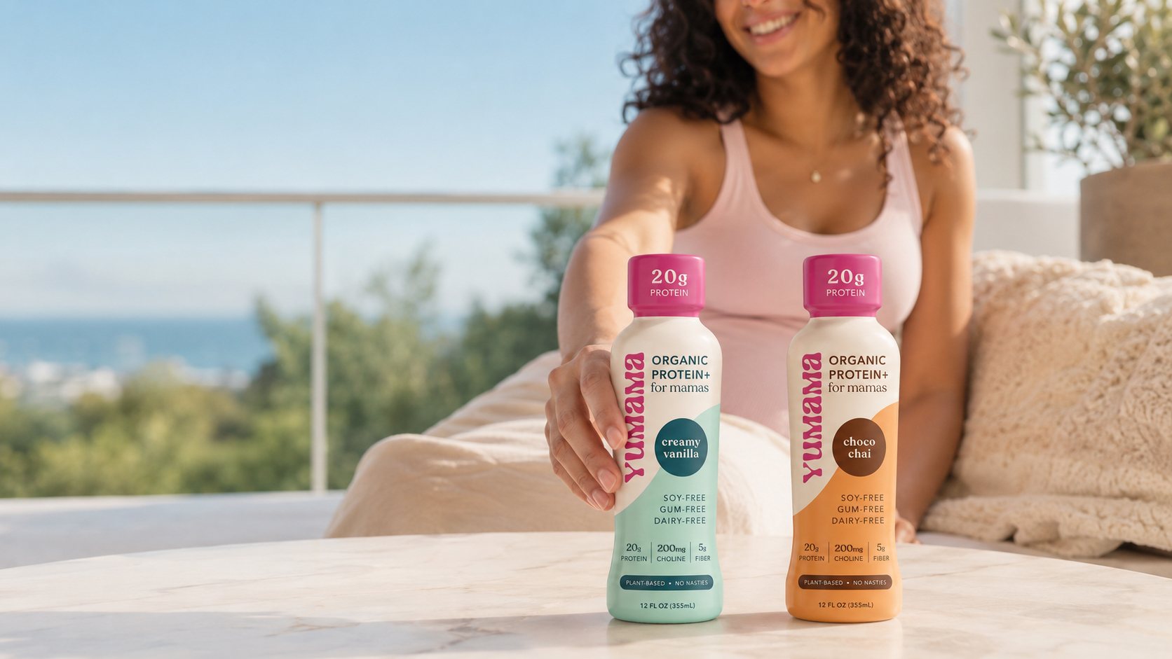 A woman reaching for a Yumama bottle on a table, creamy vanilla and choco chai side by side.